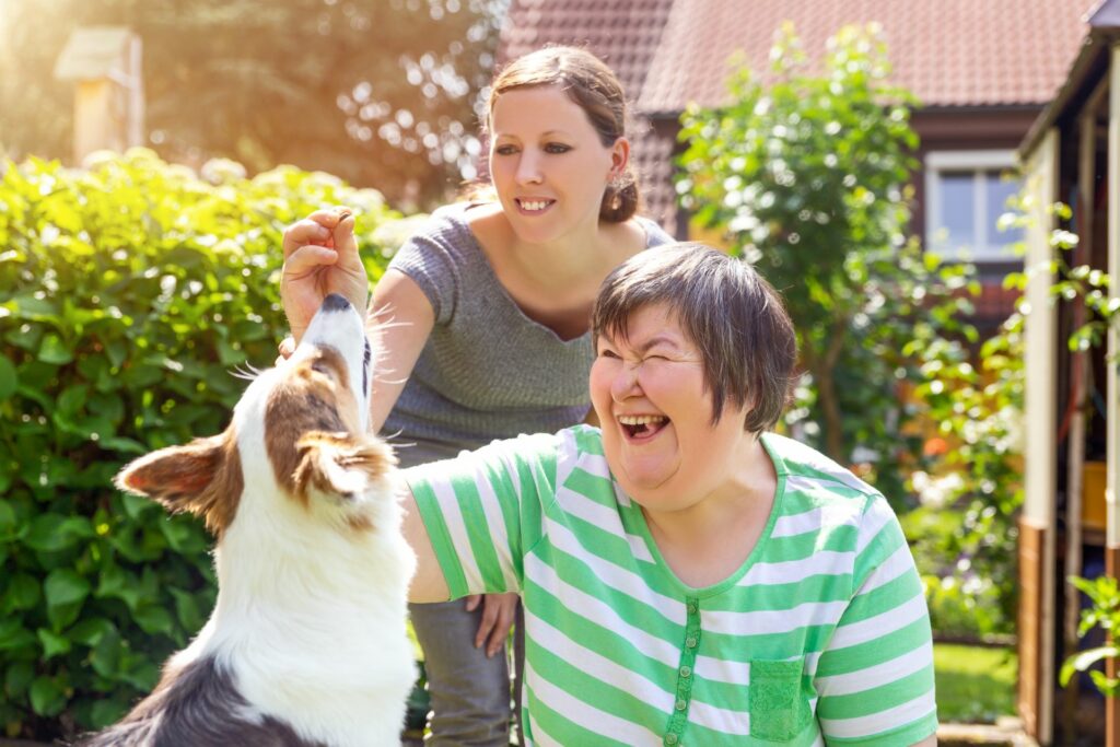 A woman gives treats to a dog while her support worker watches on.